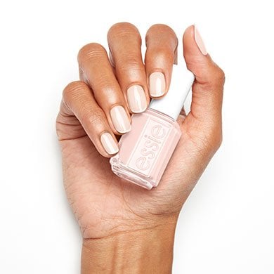 A hand with neatly manicured nails holds a bottle of light pink nail polish against a white background, conveying a clean and polished look.