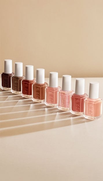 Seven nail polish bottles in shades ranging from dark brown to light pink are lined up on a beige surface.