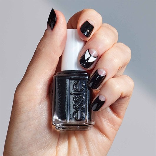 light skin hand with goth girl nail art holding a bottle of black essie nail polish