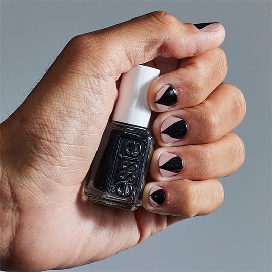 close-up of a light skin hand with werewolf nail art holding a bottle of black essie nail polish