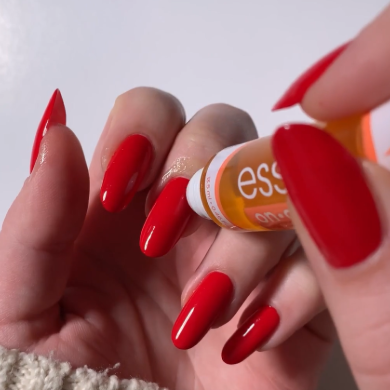 A person applying cuticle oil to hands with painted red nails