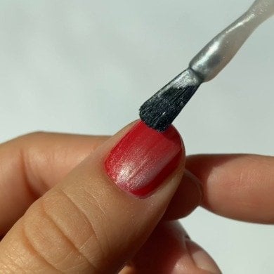 Hand with green nails holds an Essie nail polish bottle. The polished nails match the bottle color, set against a plain white background.