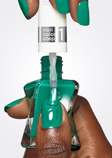 Dark skin hand holding an open bottle of green gel nail polish brushing it on the thumbnail