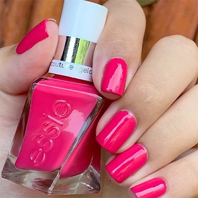 Light skin hand holding a bottle of bright pink gel couture nail polish with all five nails painted