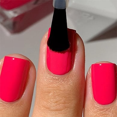 Closeup of three light skin fingernails with one being brushed with clear gel top coat