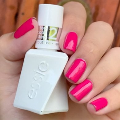 Light skin hand holding a white bottle of gel couture matte top coat wearing pink gel nail polish
