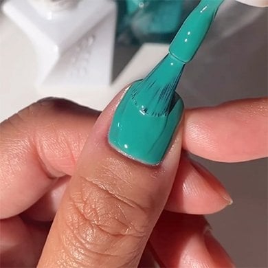 Light skin thumb getting a second coat of green essie longwear polish brushed on