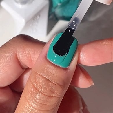 Closeup of light skin thumb wearing mint green polish getting clear top coat brushed on