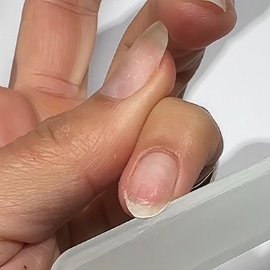 Medium skin hand nude nails with pinky folded down getting filed on the side with a gray file