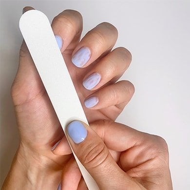 Light skin hands, one filing off the surface of a gel nail with a white nail file.