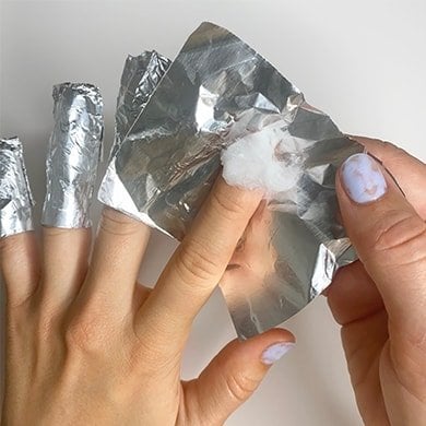 Fingertip covered in an acetone-soaked cotton ball and a foil wrap about to be applied.
