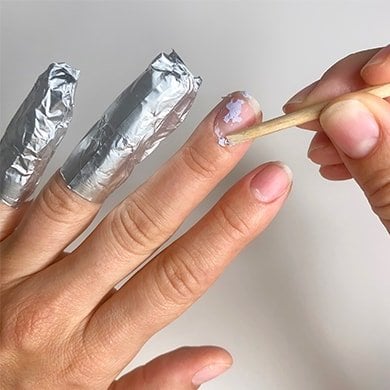 Flakes of gel nail polish being pushed off a nail with an orangewood stick.