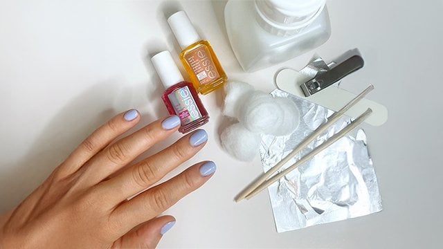 Light skin hand next to two bottles of nail treatment and supplies to remove gel nail polish