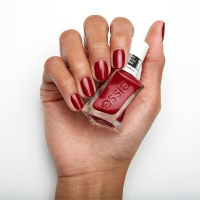 A hand with neatly manicured nails holds a bottle of red nail polish against a white background, conveying a clean and polished look.