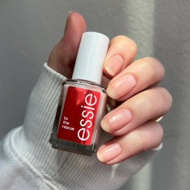 A hand holding a bottle of Essie to the rescue uv gel damage repair. The nails are natural. .