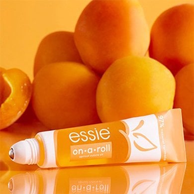 Roll on essie cuticle oil in front of a pile of apricots on an orange table