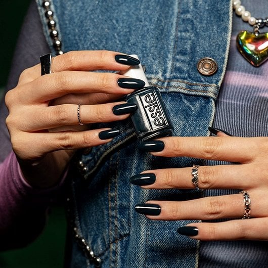 Model with a navy blue manicure and statement rings holding a bottle of essie nail polish