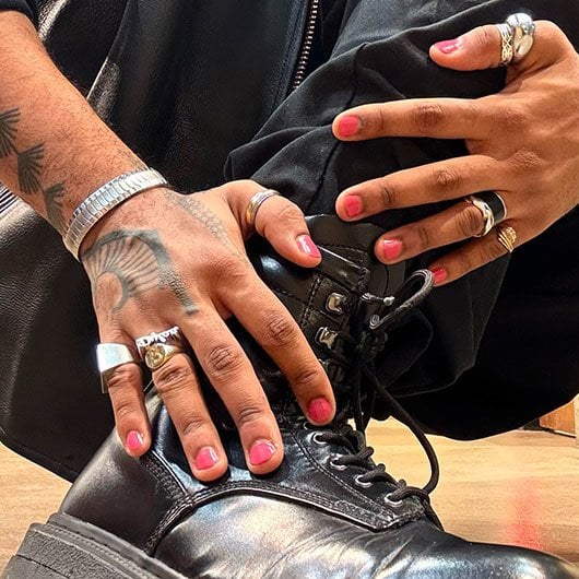 Model wearing pink manicure and statement rings placing hands over top their shin and leather boot